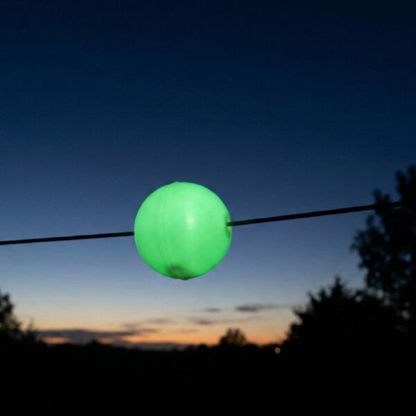 A photograph taken at twilight shows a spherical glow-in-the-dark bird flight diverter glowing green on a power line.
